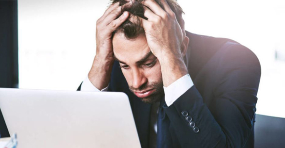 A man in a suit looking stressed at a laptop.