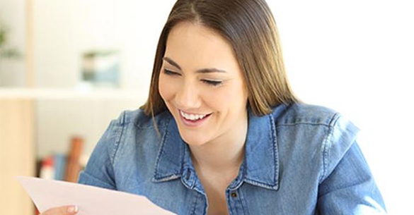 A female smiling while looking at a piece of paper in her hand.