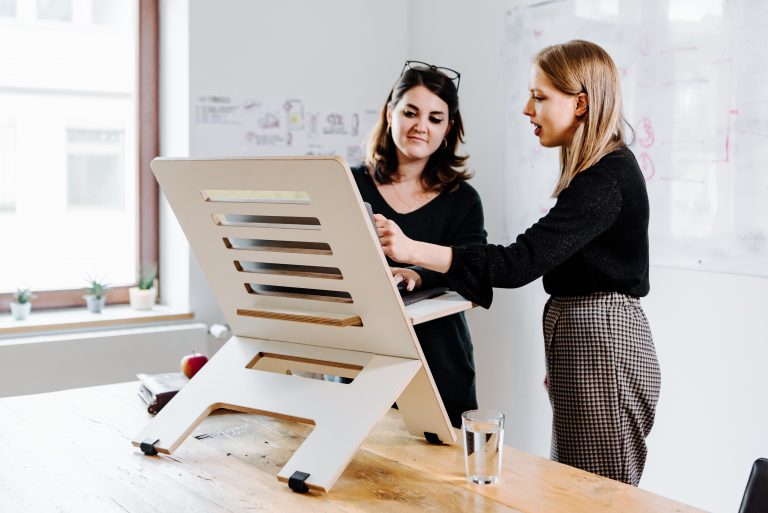 Two business women standing and looking a laptop on a height adjustable platform.
